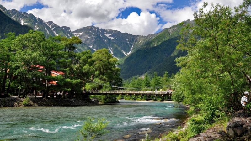 A suspension bridge spans the Azusa River in Kamikochi with the Japanese Alps behind.