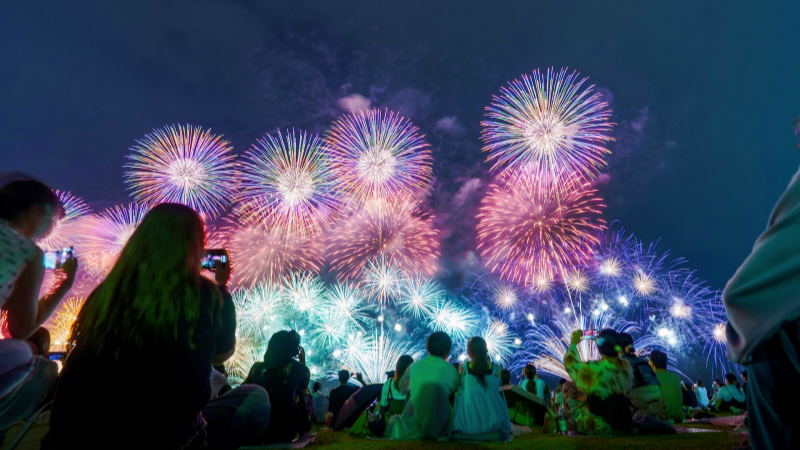 Crowds sit on picnic mats watching a dazzling fireworks festival in Japan.