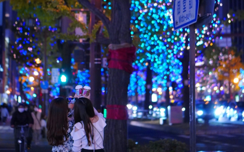 Friends capturing a moment under the dazzling blue and purple winter lights of Osaka's Mido-suji.
