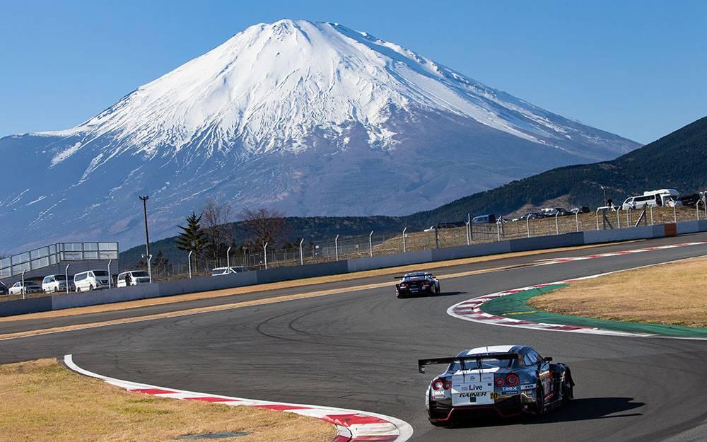 Race cars speed around the iconic Fuji Speedway track backed by the breathtaking snow-capped peak of Mount Fuji